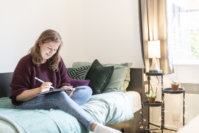 Student writes whilst sat on bed