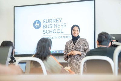 MBA lecturer standing in front of screen with Surrey Business School logo and in front of seated students