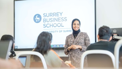 MBA lecturer standing in front of screen with Surrey Business School logo and in front of seated students