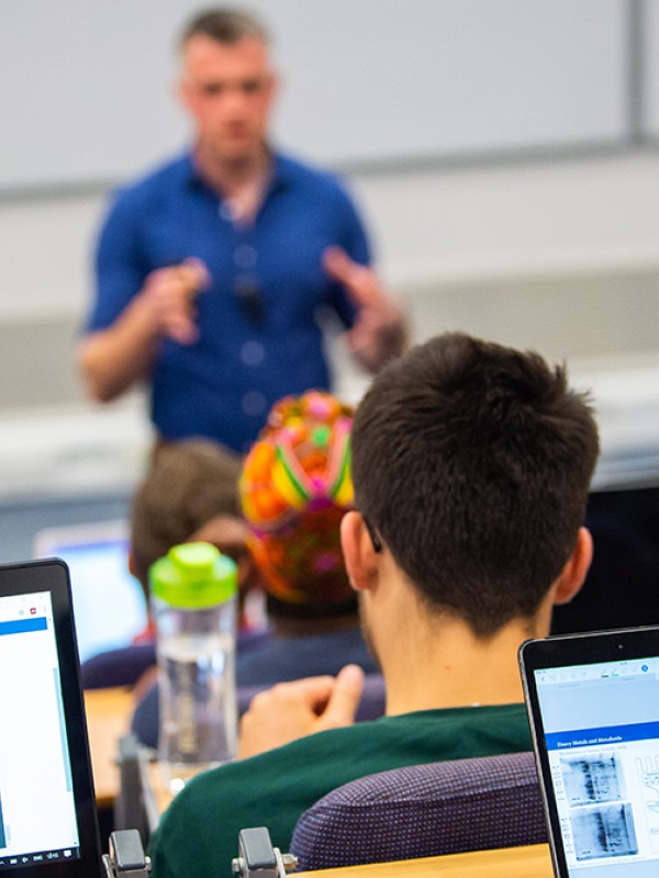 Biochemistry students are sitting a lecture, their laptops are open and a lecturer is speaking