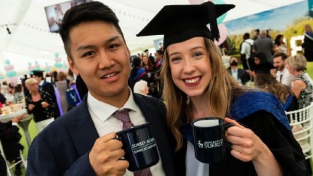 Male and female graduate holding Surrey mugs