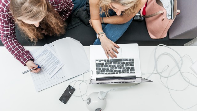 An overhead view of two students working on a laptop with a notepad