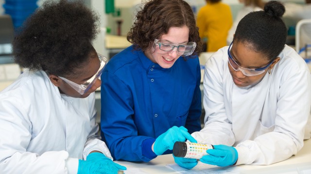Two students watching a member of staff pointing to a pH scale on the side of a bottle