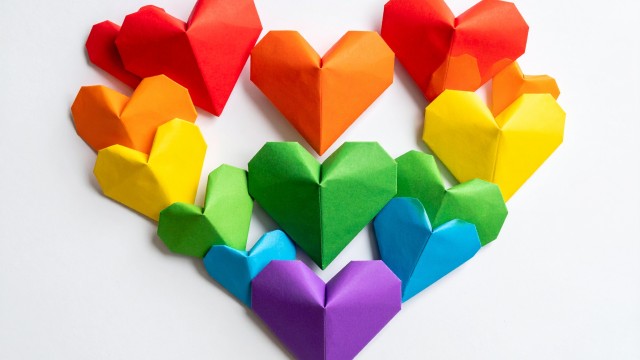 rainbow of origami hearts laid out in a heart shape on a white table 