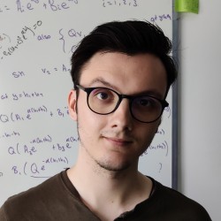 Ryan stands in front of a white board with equations, smiling at the camera.