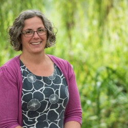 Woman standing with short curly brown and grey hair, wearing glasses