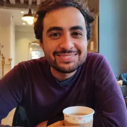 Colour image of Ihsaan facing the viewer with a smile and coffee cup in hand.