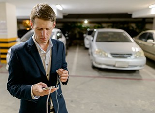 A man is looking at his phone in front of a silver car