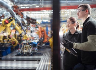 People observing a robotic production line in a car factory