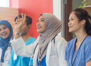 A group of Malaysian medical staff having a meeting. It is a medical team with four people from different ethnic backgrounds attending a medical conference. A Muslim female doctor raises her hand