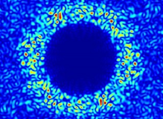 A blue circle with lighter blue pattern around it which shows light scattering from a thin silicon membrane