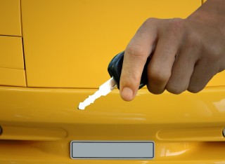 Image of person holding a car key in front of a yellow car