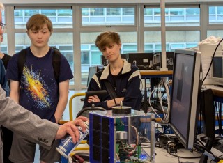 professor craig underwood demonstrating freeze spray on a satellite with students 