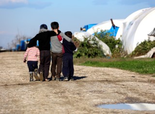 A group of refugee children with their arms around each other walking