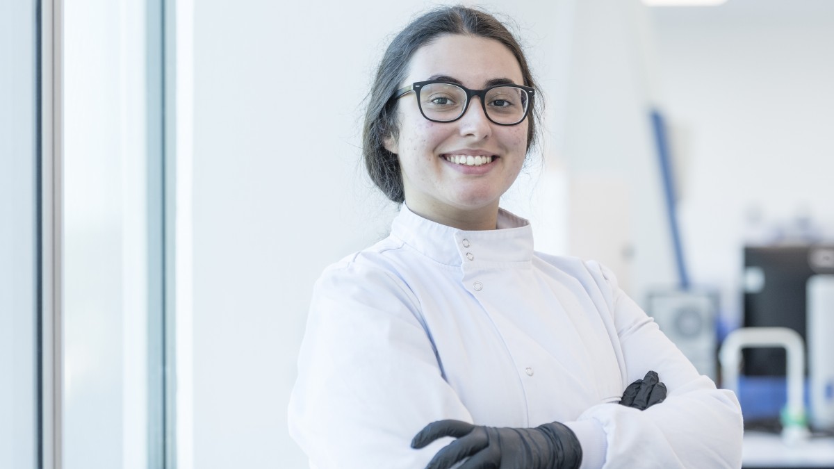 A biosciences student wearing glasses smiles confidently at the camera with her arms crossed.